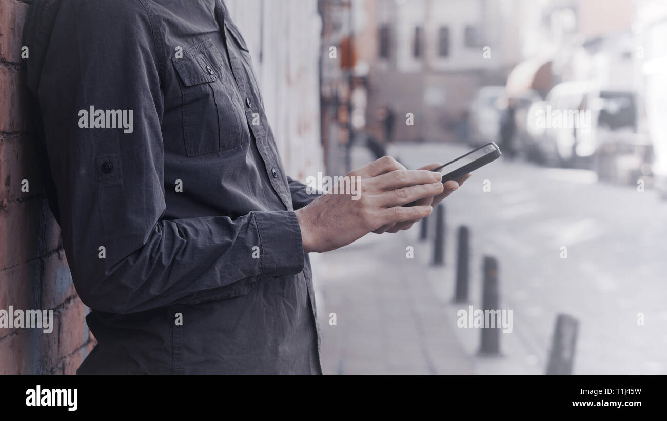 Giovane uomo in piedi contro un muro di sfondo e utilizza lo smartphone. Tecnologia e stile di vita del concetto. Foto Stock