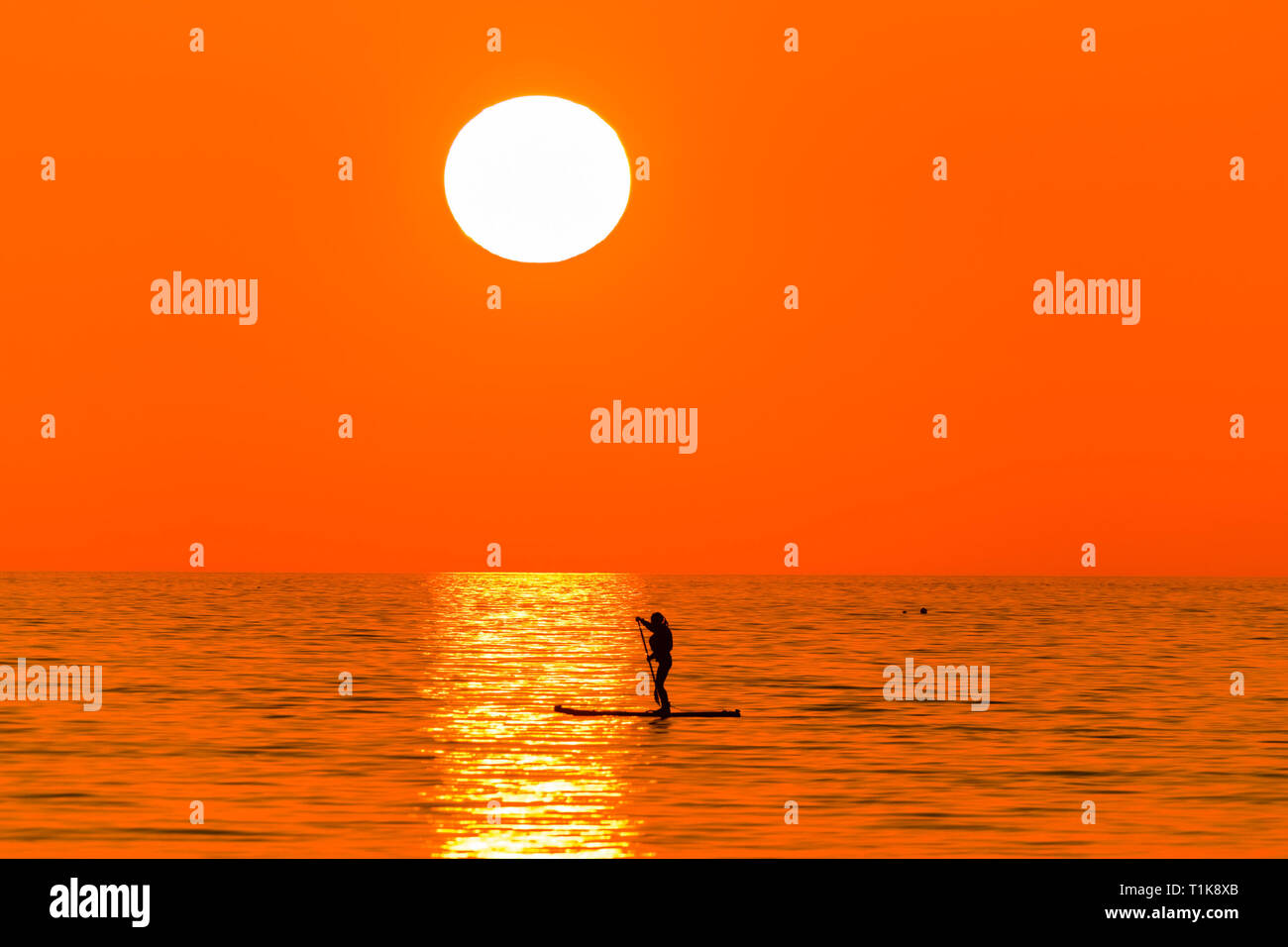 Aberystwyth Wales UK, Mercoledì 27 Marzo 2019 UK Meteo: un bel tramonto , alla fine di un altro giorno di caldo sole primaverile, sagome una persona paddleboarding su te calma piatta mare a Aberystwyth, il Cardigan Bay costa del Galles occidentale. Alta pressione continua a dominare il meteo per gran parte del Regno Unito, con condizioni regolate e chiaro quasi limpido cielo blu foto Keith Morris/Alamy Live News Foto Stock