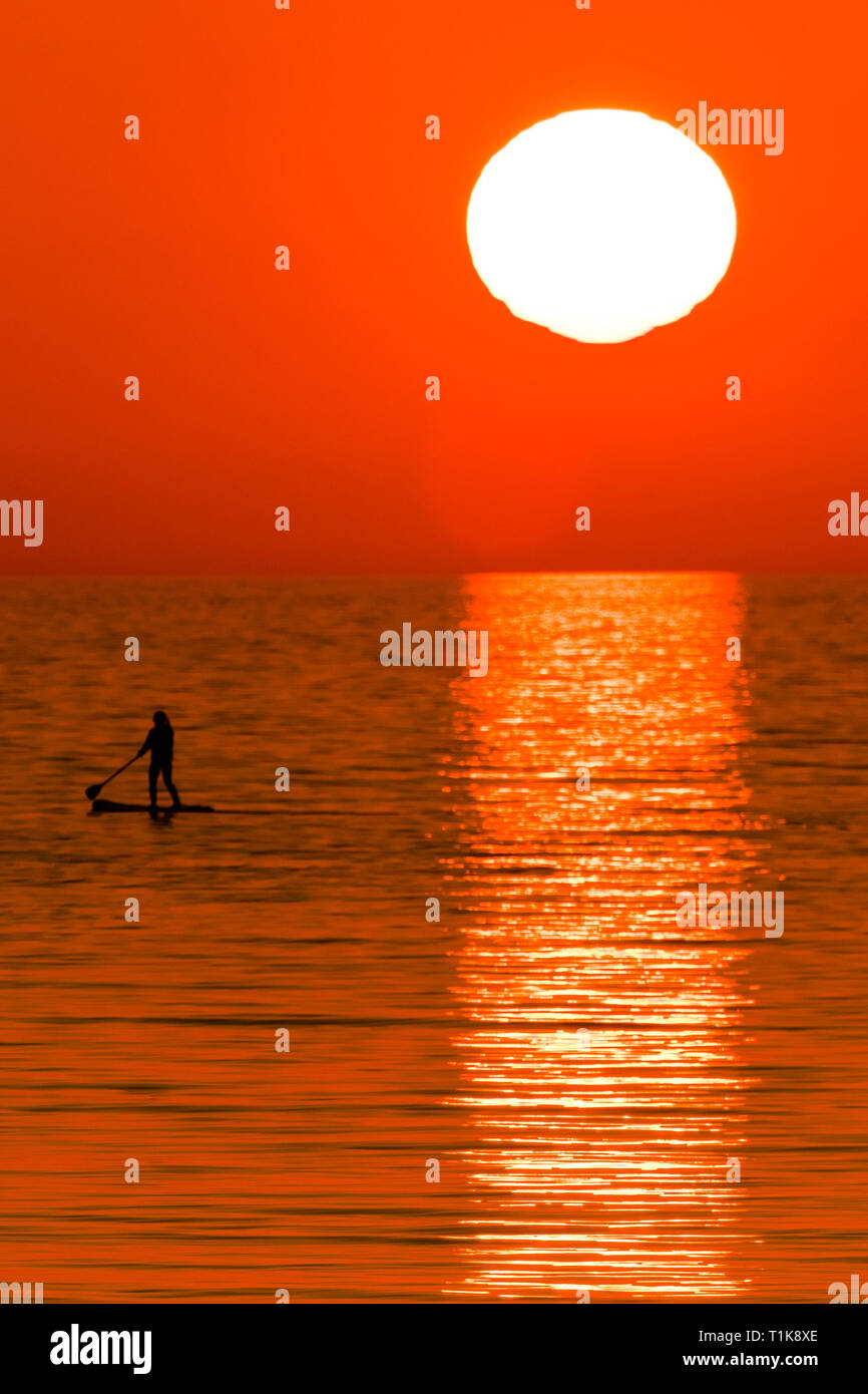 Aberystwyth Wales UK, Mercoledì 27 Marzo 2019 UK Meteo: un bel tramonto , alla fine di un altro giorno di caldo sole primaverile, sagome una persona paddleboarding su te calma piatta mare a Aberystwyth, il Cardigan Bay costa del Galles occidentale. Alta pressione continua a dominare il meteo per gran parte del Regno Unito, con condizioni regolate e chiaro quasi limpido cielo blu foto Keith Morris/Alamy Live News Foto Stock