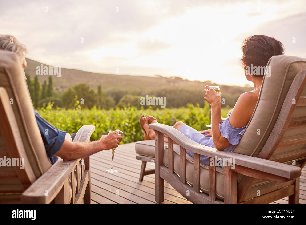 Giovane rilassante, bevendo champagne sulle sedie a sdraio sul soleggiato patio resort Foto Stock