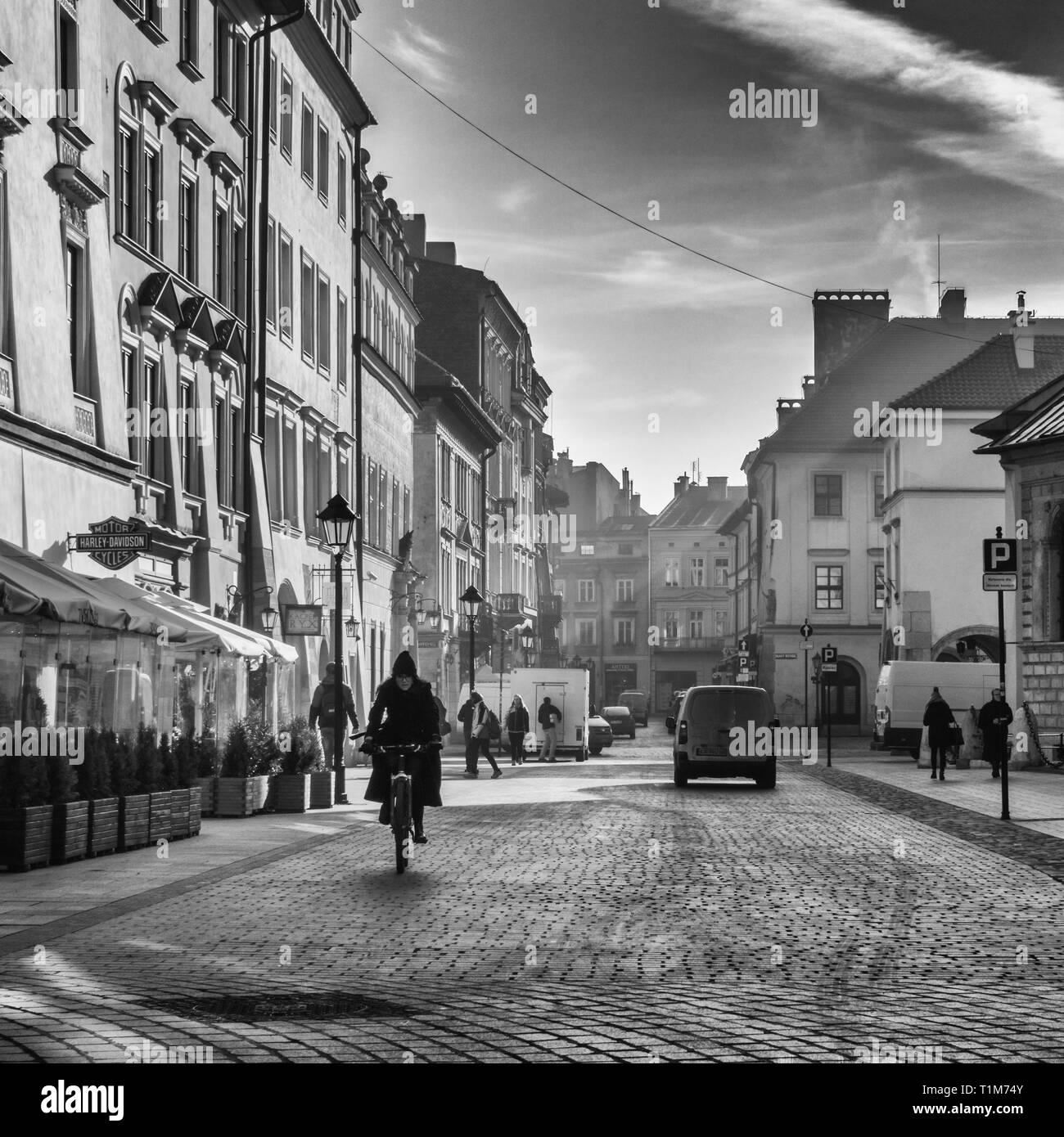 Donna locale di una bicicletta giù plac maryacki nelle prime ore del mattino con drammatica raggi del sole, Cracovia Polonia Foto Stock