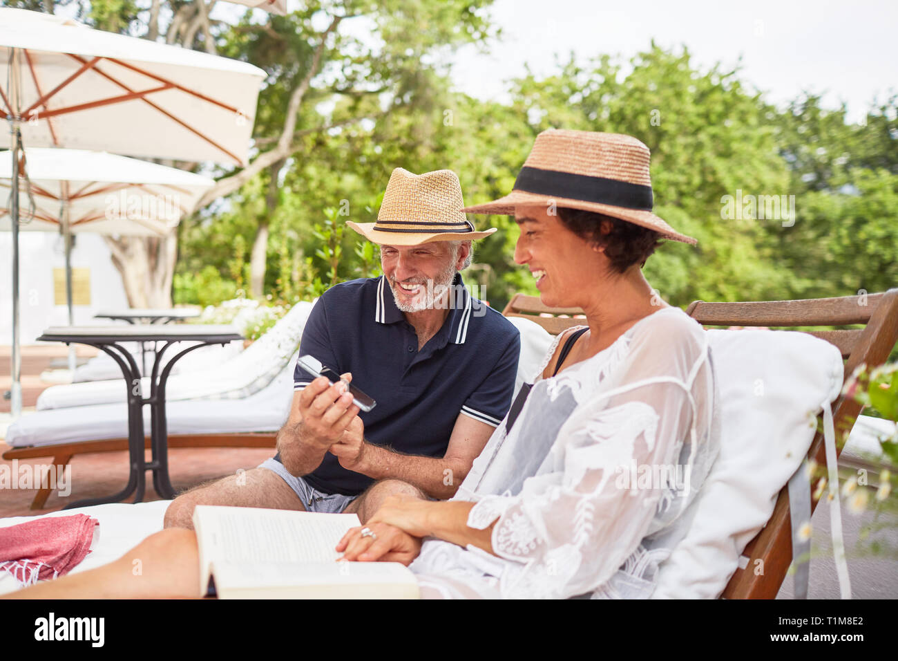 Coppia matura con smart phone rilassarsi sulle sedie a sdraio alla piscina resort Foto Stock
