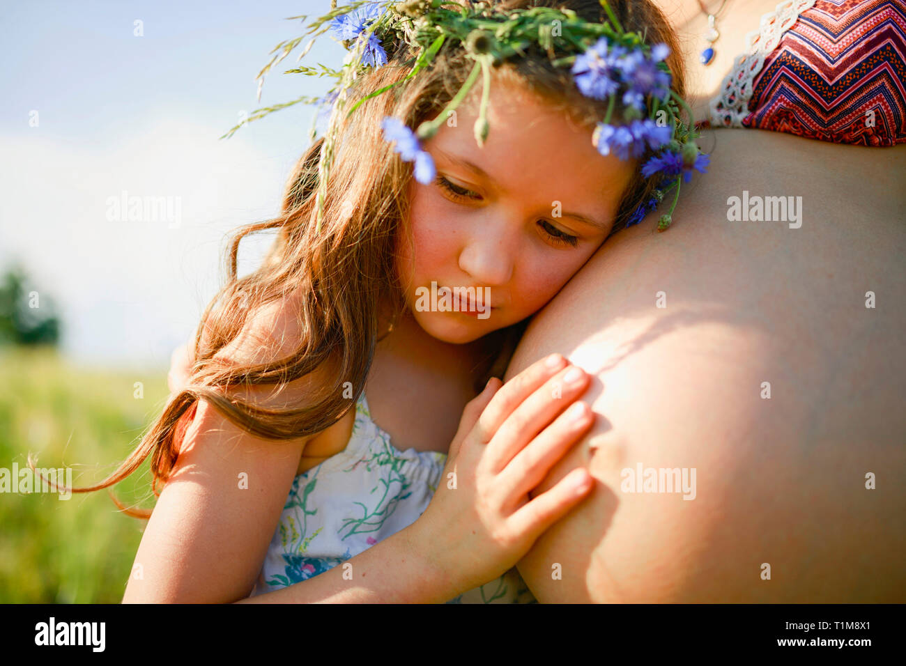 Ragazza serena con fiori in capelli appoggiati sullo stomaco delle madri incinte Foto Stock