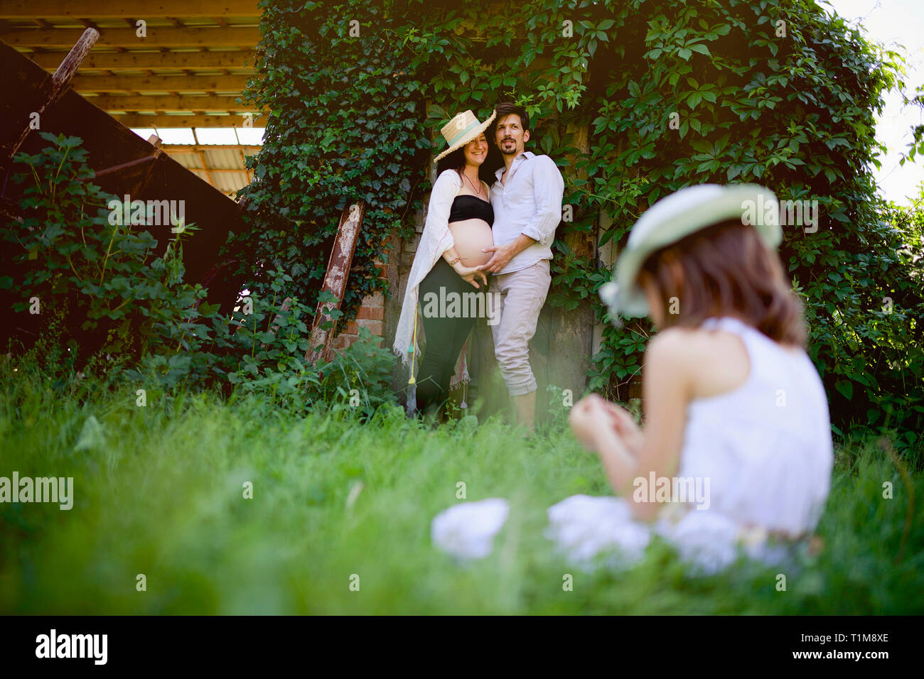Coppia incinta che guarda la figlia seduta in erba Foto Stock