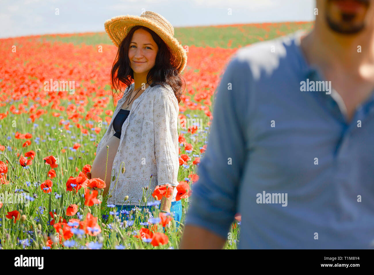 Ritratto sorridente donna incinta in piedi in un campo di papavero rosso soleggiato, rurale Foto Stock