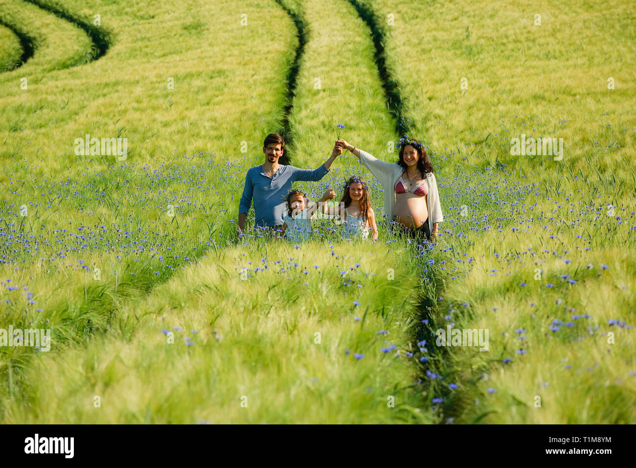 Ritratto famiglia incinta in un campo verde rurale soleggiato e idilliaco con fiori selvatici Foto Stock