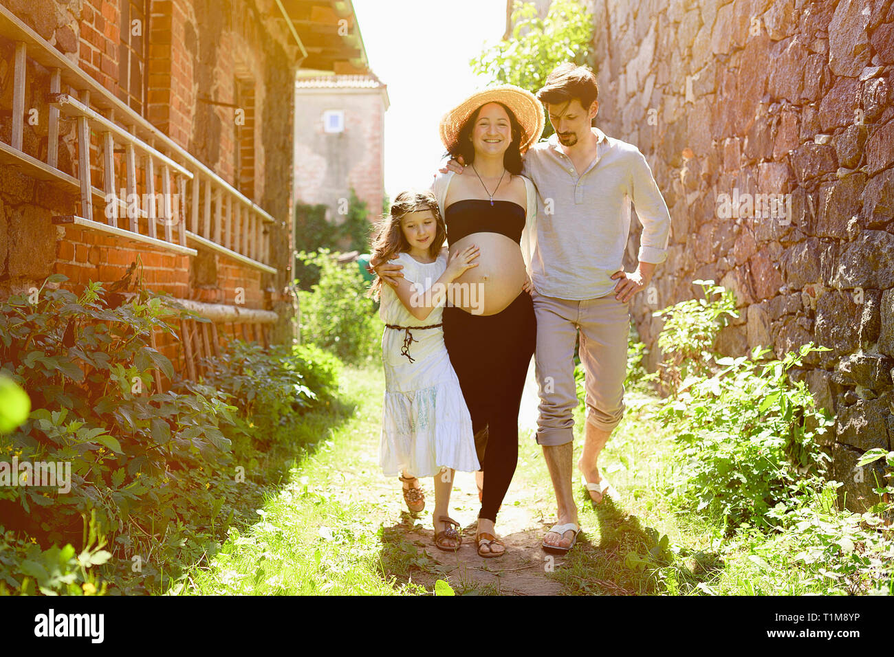 Famiglia incinta a piedi lungo la soleggiata casa colonica Foto Stock