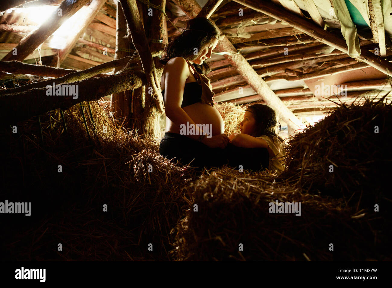 Madre incinta e figlia in loft rurale di fieno Foto Stock