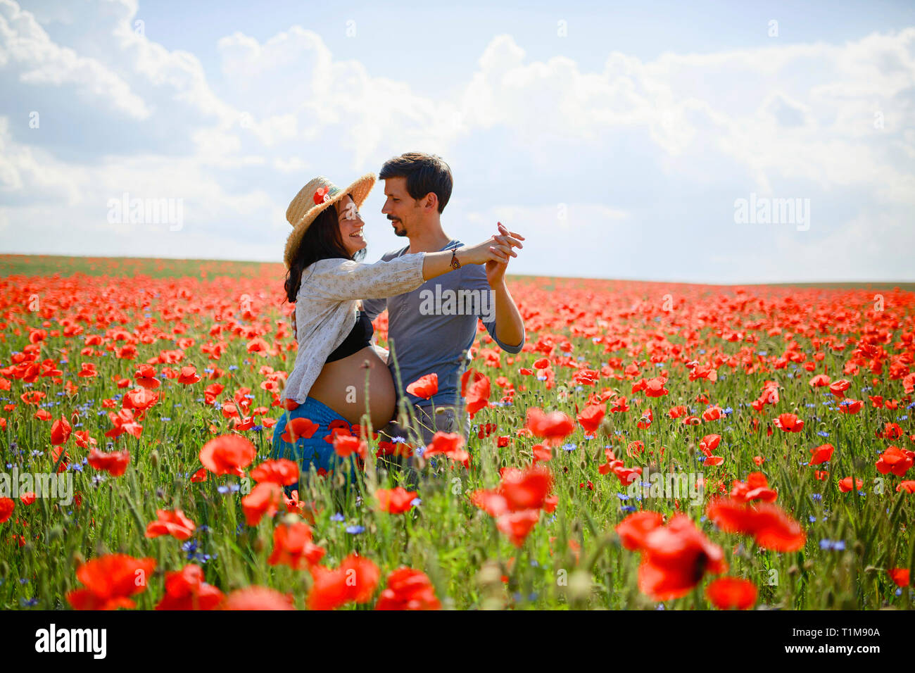 Una coppia incinta che danzano in un campo di papavero rosso soleggiato e idilliaco Foto Stock