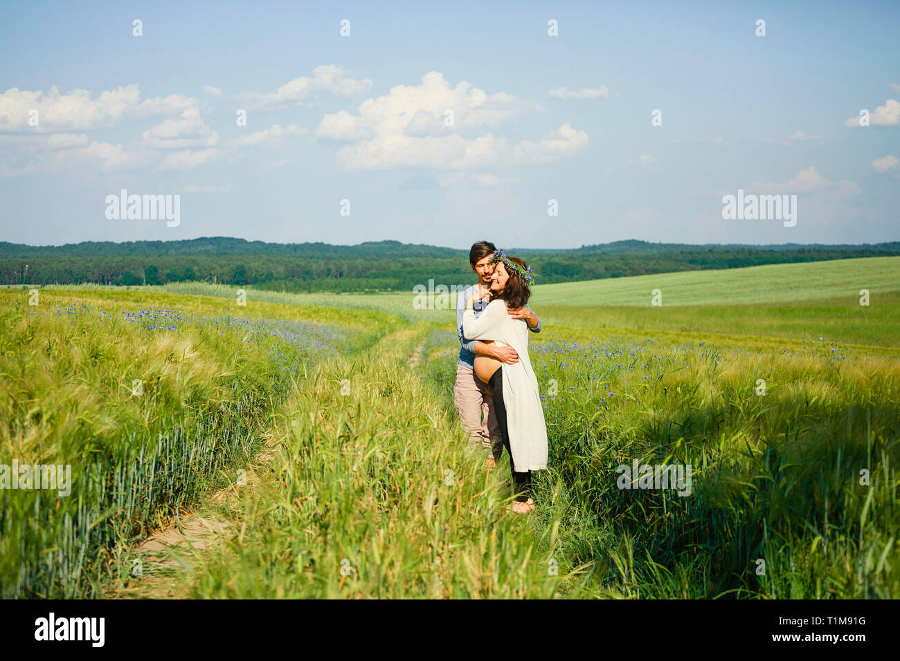 Affettuosa coppia incinta abbracciando in un soleggiato, idilliaco campo rurale verde Foto Stock
