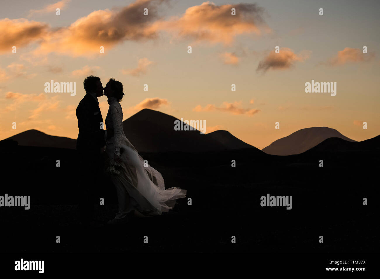 Silhouette sposa e sposo che si baciano al tramonto con montagne tranquille sullo sfondo Foto Stock