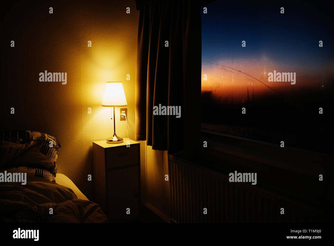 Comodino illuminante angolo camera da letto accanto alla finestra con vista del tramonto Cielo Foto Stock