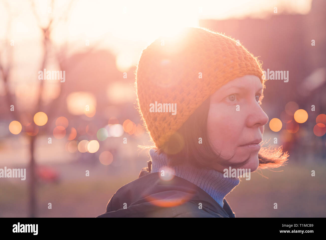 Ritratto di donna bella in 40s contro la luce del sole di autunno nel parco, persona di sesso femminile che indossa il cappuccio giallo cercando in distanza Foto Stock