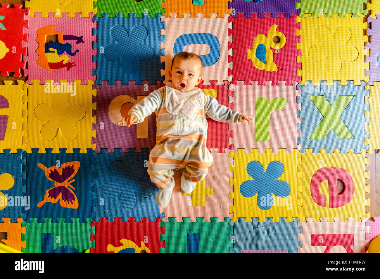 Adorabili e sorridente baby visto dal di sopra in pigiama, stare sdraiato sulla schiena nel suo giocattolo camera. Foto Stock