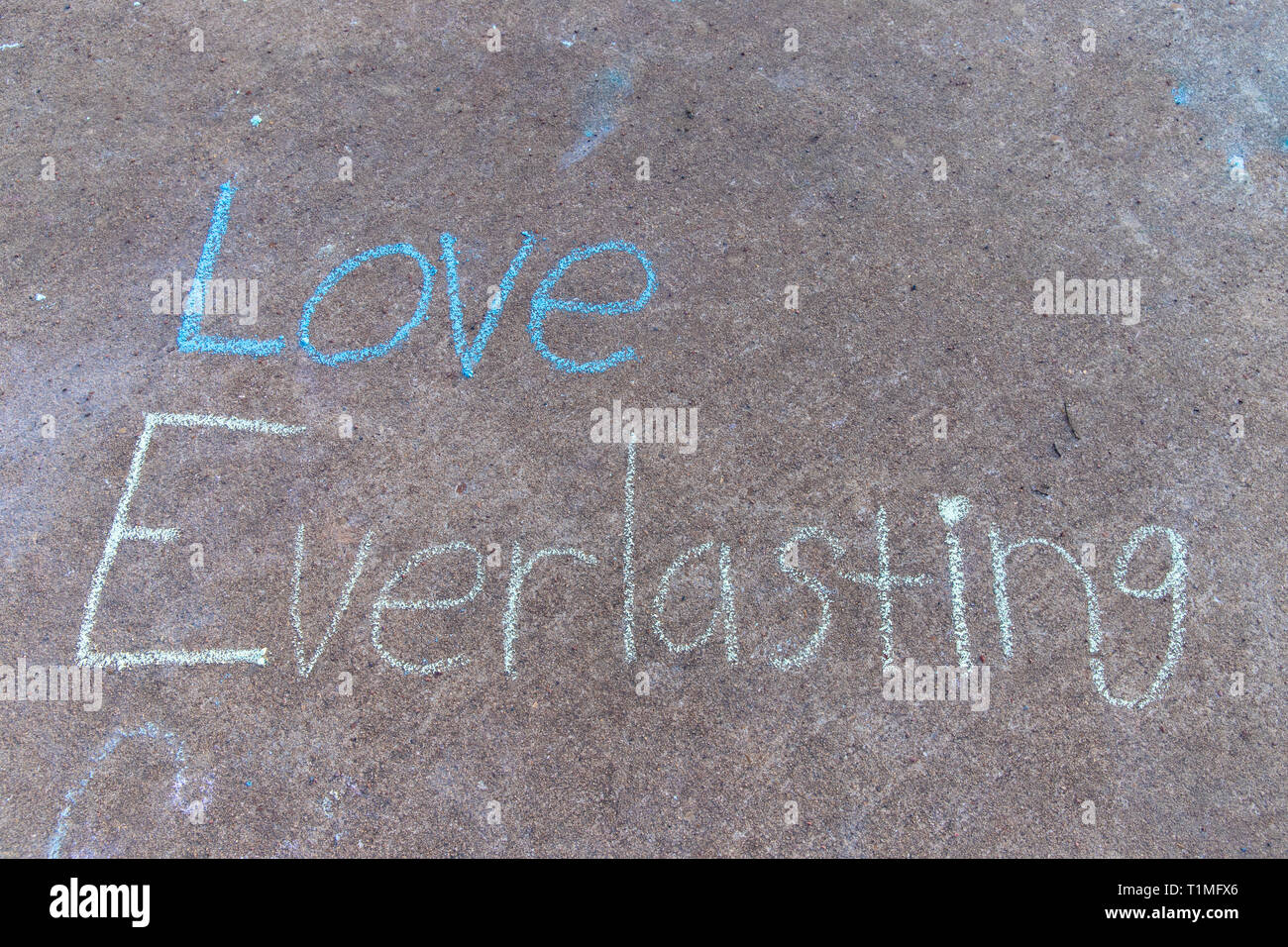 Le parole di amore eterno con scritta sidewalk chalk sul marciapiede grigio sfondo Foto Stock
