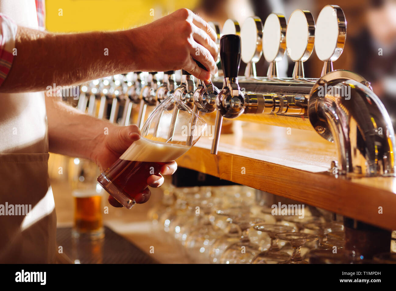 Barman indossando grembiule beige a versare birra per il suo cliente Foto Stock