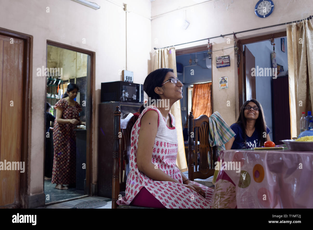 Bellissimo Indian Bengali ragazze sono avente divertente parlare al tavolo per la cena mentre la madre è la cottura Foto Stock
