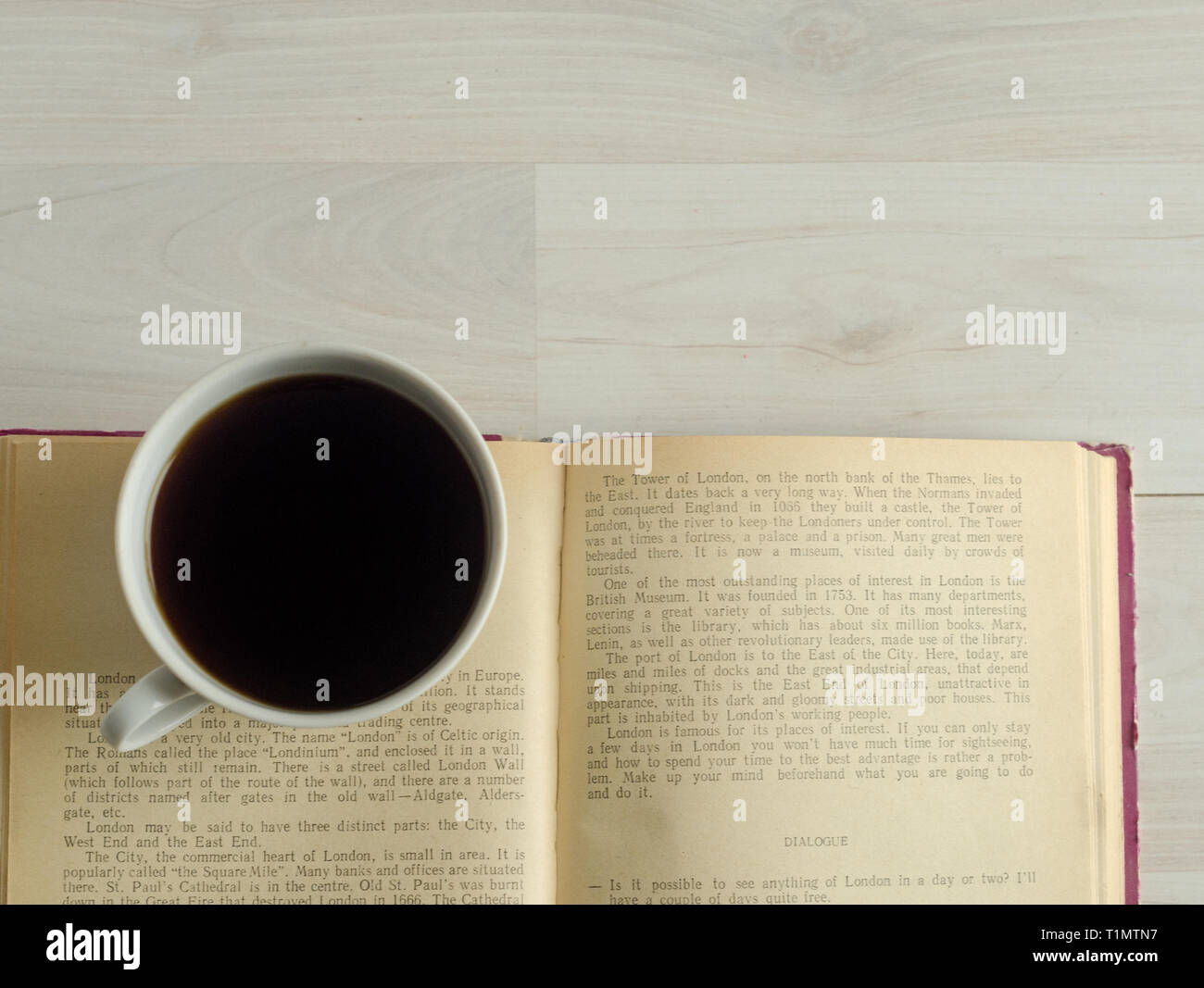 Una tazza di caffè e un libro aperto sul bianco sullo sfondo di legno. Foto Stock