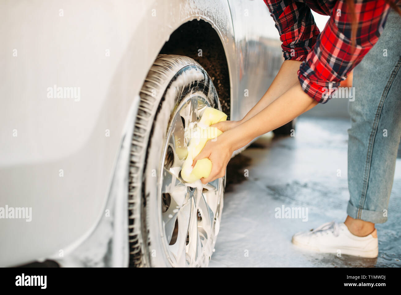 Carino donna di lavaggio delle ruote del veicolo con schiuma Foto Stock
