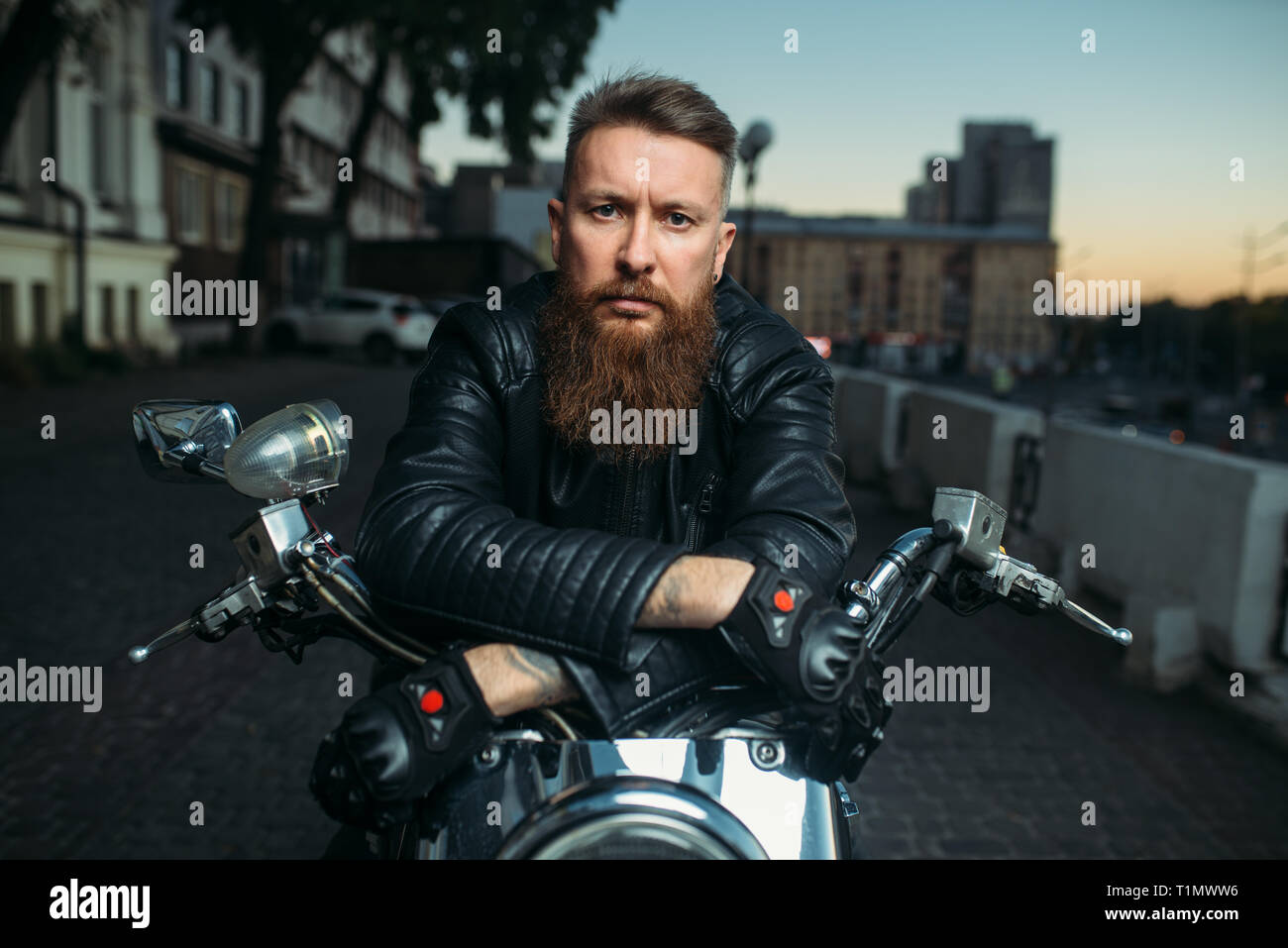 Brutale barbuto biker pone sul trinciapaglia, vista frontale Foto Stock