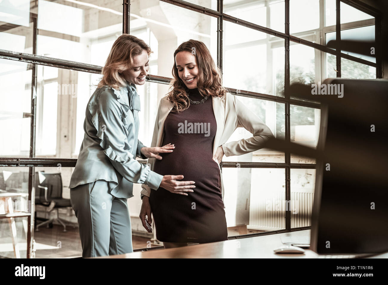 Trasmissione via IR di bionda amica sfregamento pancia incinta del suo dai capelli scuri collega Foto Stock