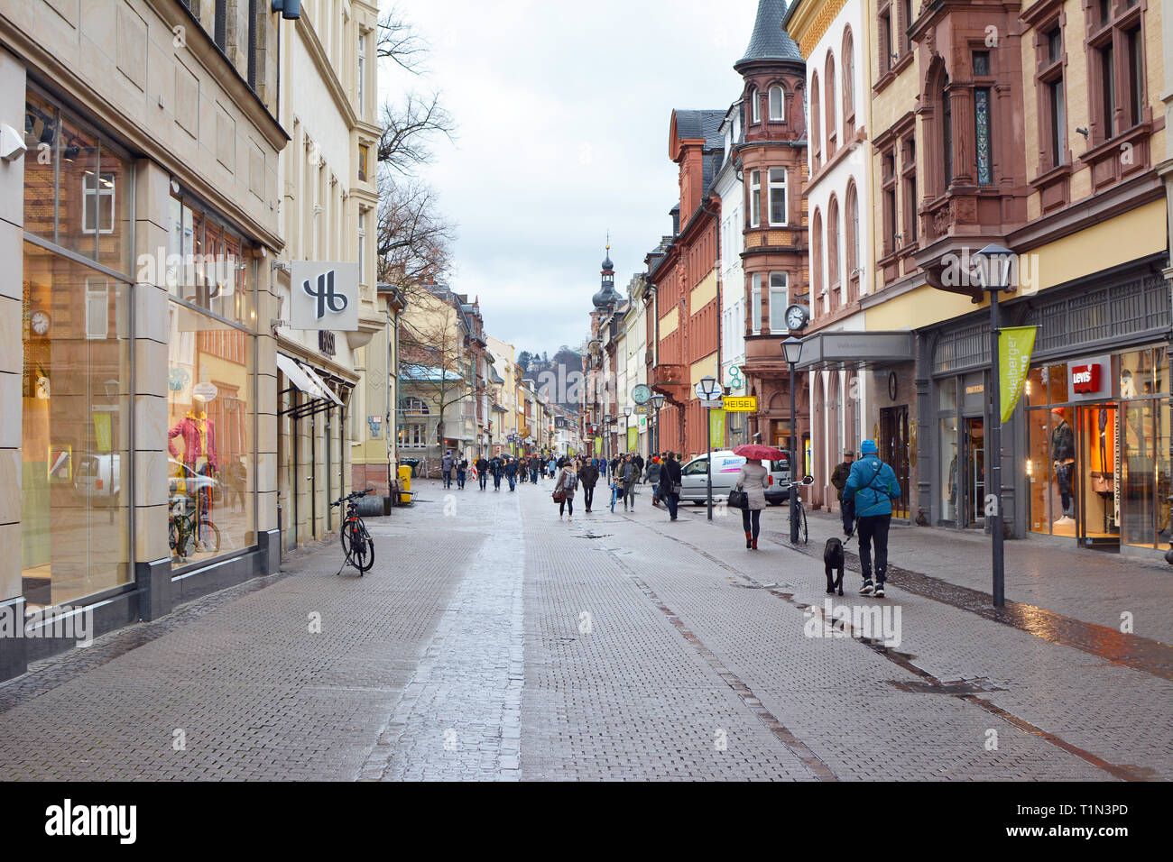 Strada principale con diversi negozi in edifici vecchi e poche persone nel centro storico della città in un giorno di pioggia in Heidelberg, Germania Foto Stock