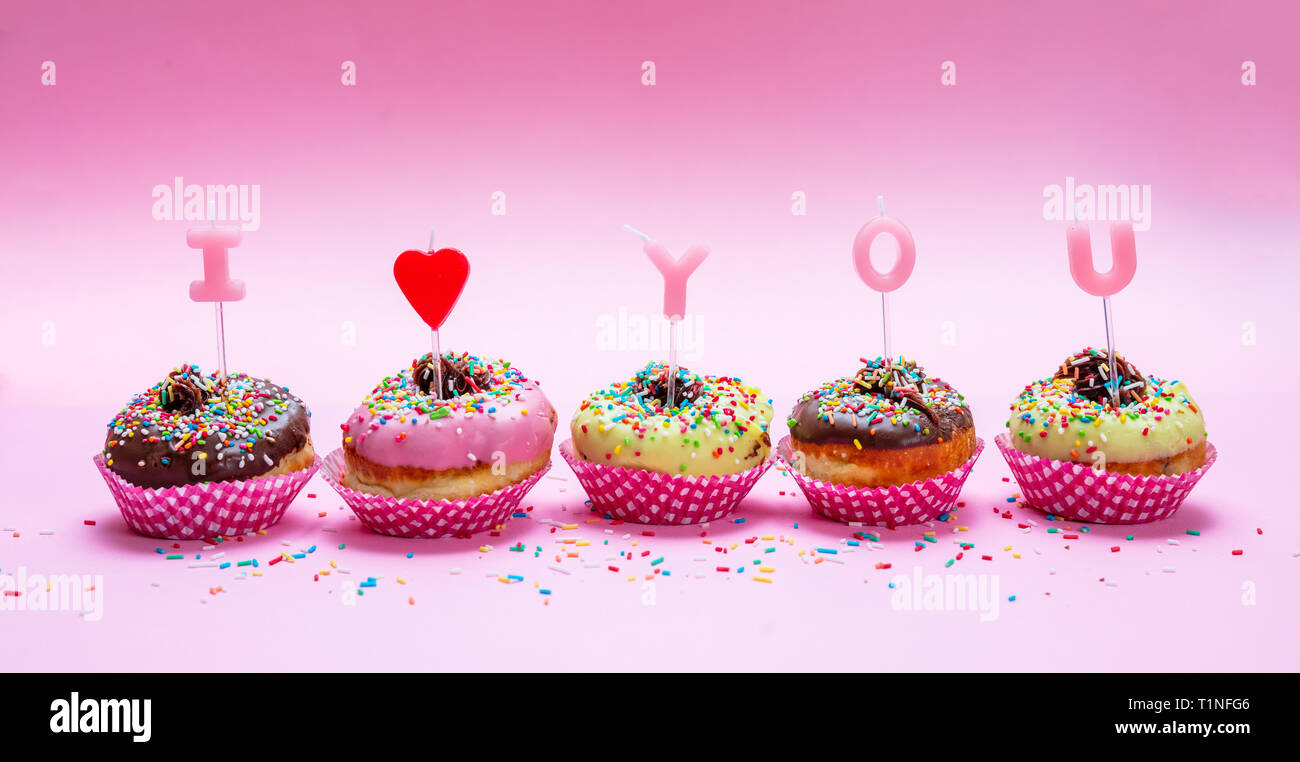 Il giorno di San Valentino. Mini torte con glassa e granelli colorati su sfondo rosa, testo ti amo, banner Foto Stock