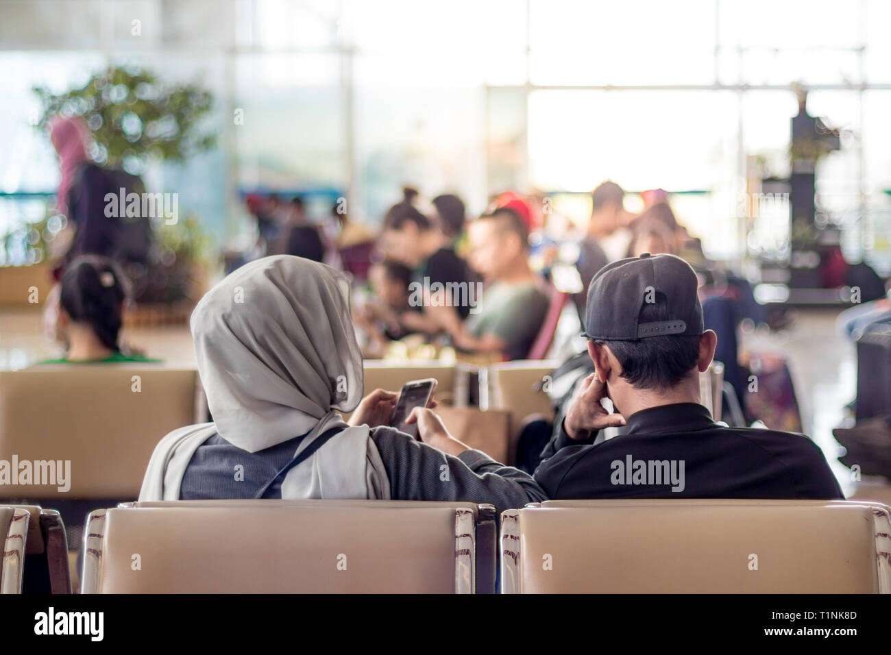 Moderno islamico musulmani asian giovane utilizzando il proprio smartphone apps seduti e in attesa di un volo in partenza a international airport terminal Foto Stock