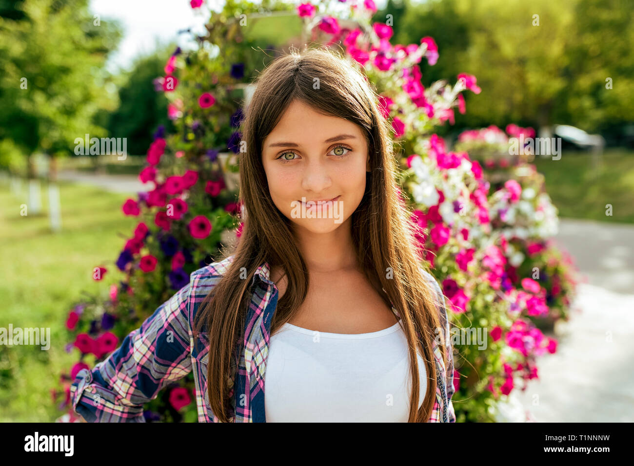 Bella ragazza adolescente 13-16 anni sullo sfondo di un letto di fiori. Felice sorrisi. In estate in città dopo la scuola. Vacanze weekend in città Foto Stock