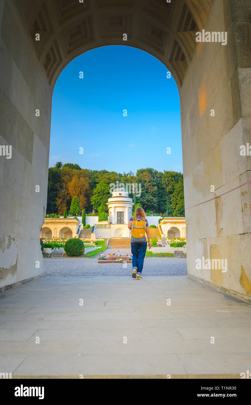 Lviv, Ucraina- Agosto 31, 2018: cimitero Lychakiv al tramonto. Giovane donna turistico con un zaino giallo passa al di sotto dell'arco Foto Stock