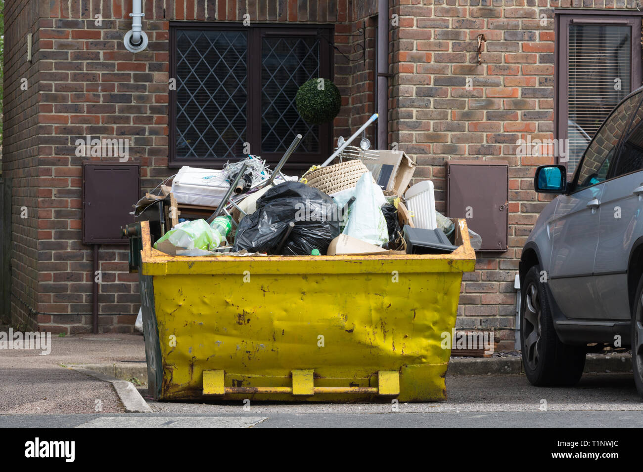 Skip giallo piena di rifiuti domestici o di rifiuti per smaltimento sul vialetto di una casa, REGNO UNITO Foto Stock