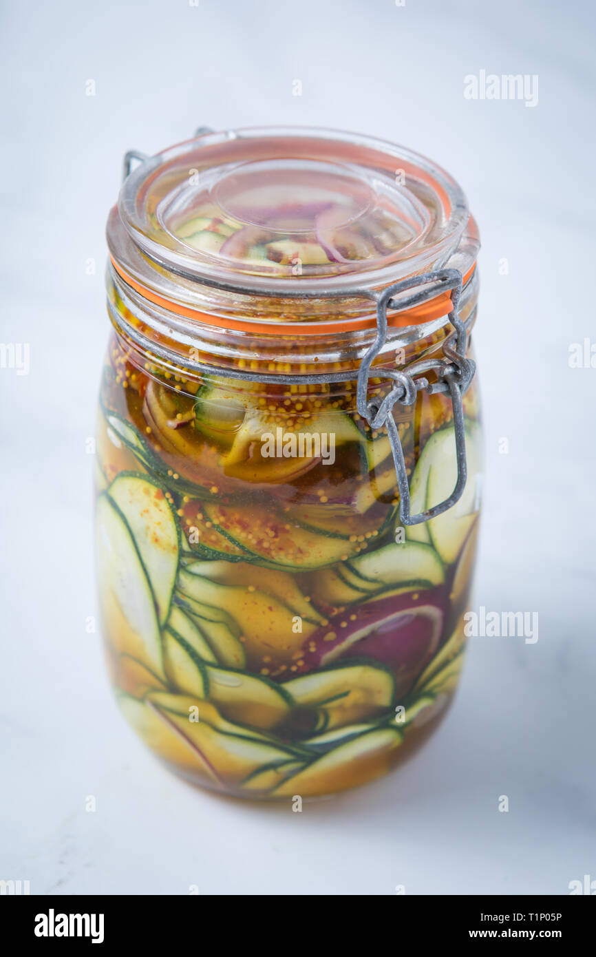 Close up di un piccante di zucchina cipolla rossa pickle marinata in un chiuso mason jar con uno sfondo bianco. Verdure sottaceto in un vaso. Foto Stock