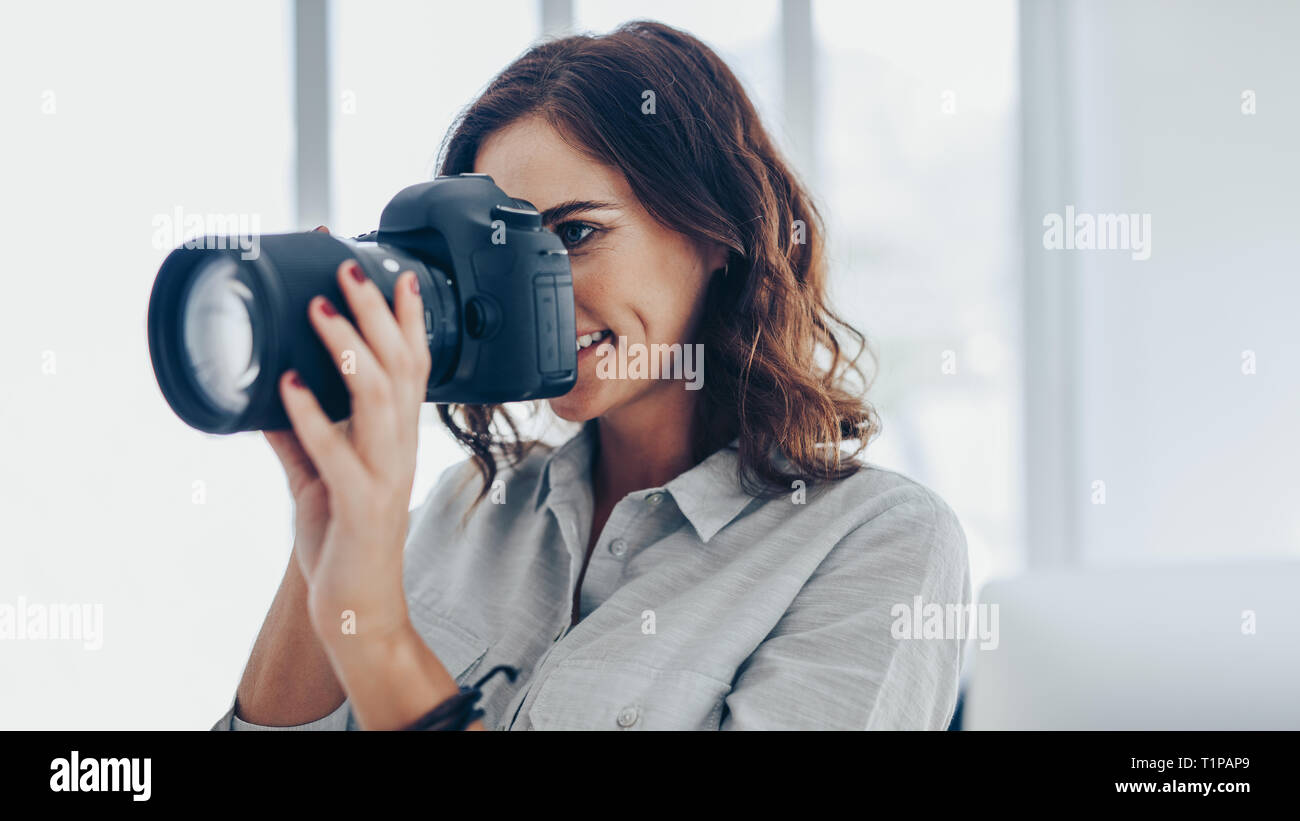 Donna con fotocamera DSLR a fotografare in interni. Femmina caucasica fotografo con la fotocamera per scattare foto. Foto Stock