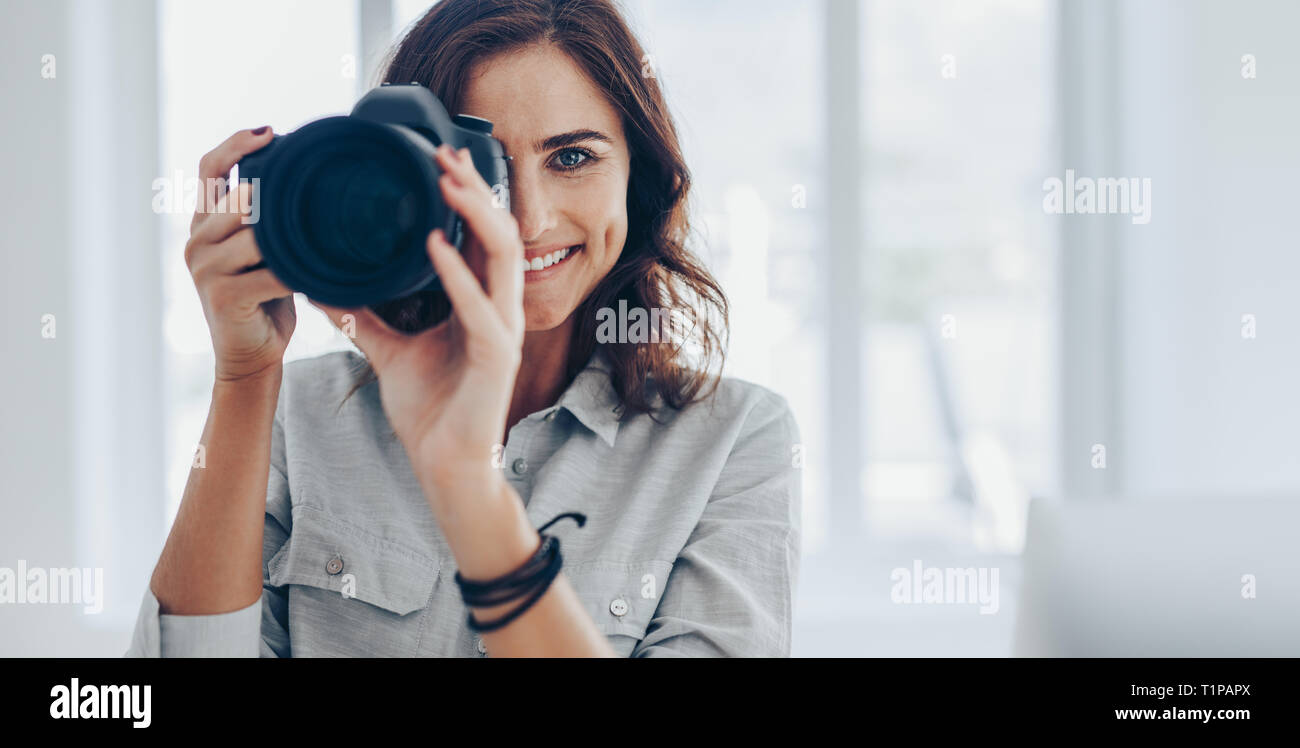 Felice giovane donna di scattare foto con la fotocamera reflex digitale in ambienti chiusi. Fotografo professionista di scattare le foto nel suo studio. Foto Stock