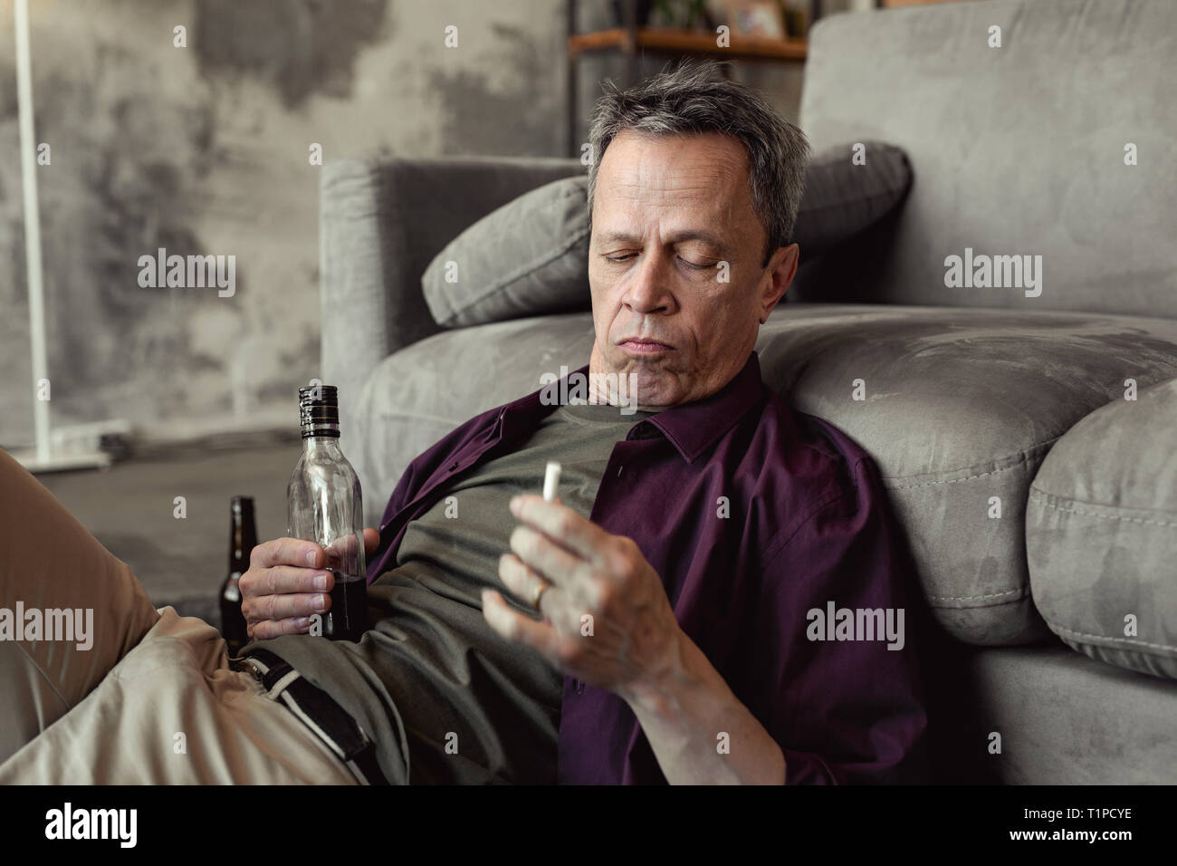 Bevuto a pelo corto vecchio uomo spendere del tempo a casa con alcool e il fumo Foto Stock