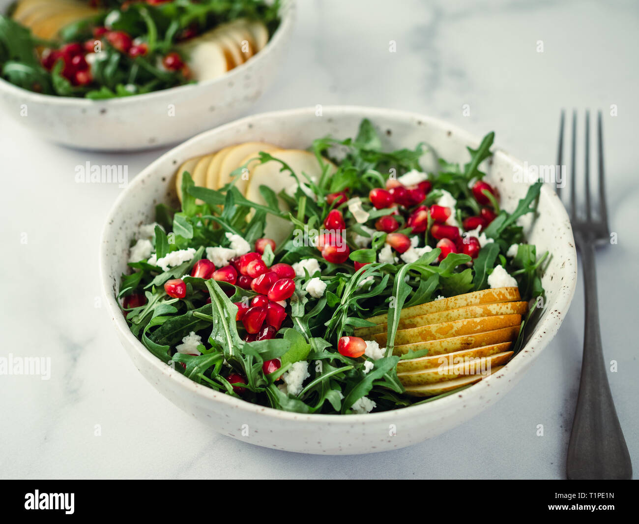 Insalata fresca con rucola, pera, melograno e noce di cocco crumble o ricotta. Due ciotole con deliziosa estate insalata di frutta sulla tavola di marmo. Copia spazio per il testo Foto Stock