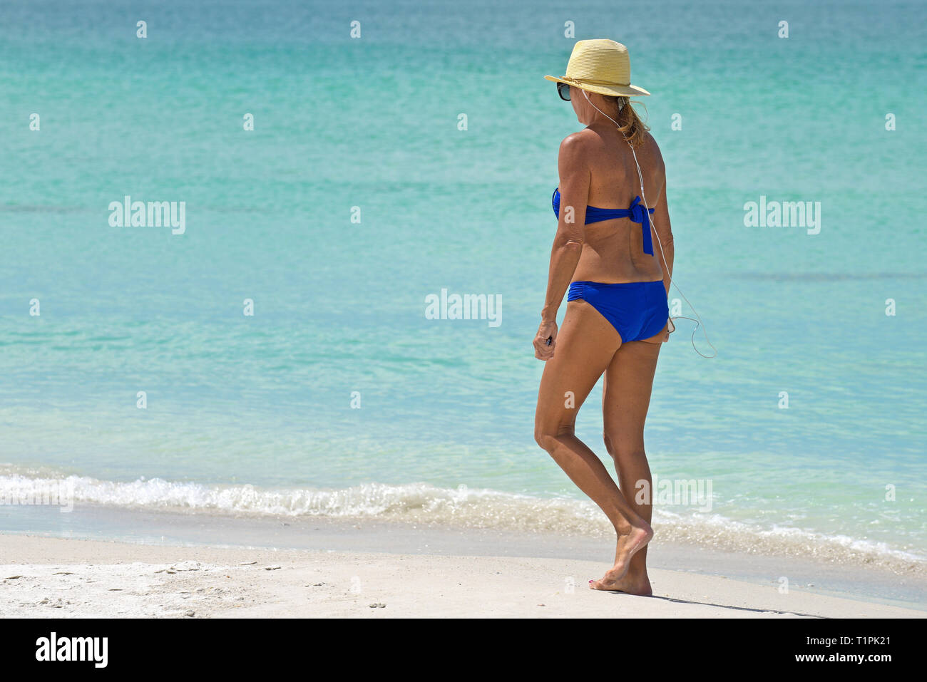 Bella donna matura indossando Bikini blu per ascoltare musica mentre facendo una piacevole passeggiata sulla spiaggia. Foto Stock