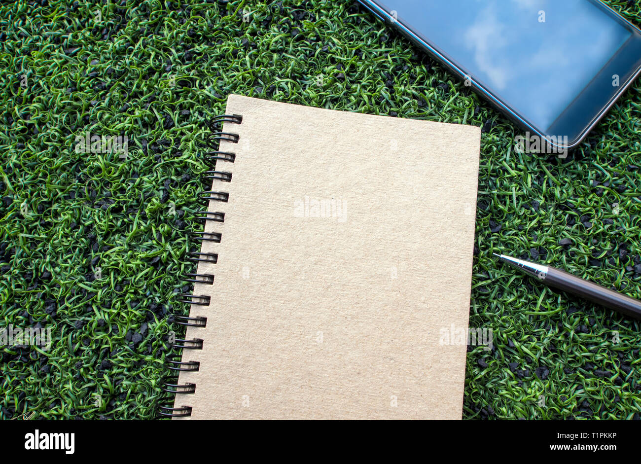 Pagina vuota di carta kraft notebook a spirale con la penna sulla trama di erba artificiale Foto Stock