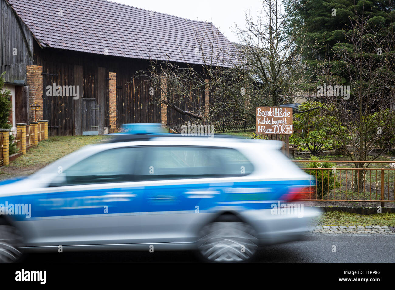 28 marzo 2019, in Sassonia, Mühlrose: Vista su una macchina della polizia in un giardino frontale del villaggio Mühlrose nella Lausitz, in cui un cartello con la scritta "si seppellire il carbone, si seppellire il nostro paese". Mühlrose è uno degli ultimi villaggi del distretto Lusatian per dare modo a carbone marrone, che è quello di essere dragati all inizio del 2030s. Lausitz Energie Bergbau AG si aspetta un volume di produzione di 150 milioni di tonnellate di carbone. Il nuovo mulino rose si trova quindi nel ciclo di sette chilometri di distanza. Foto: Oliver Killig/dpa-Zentralbild/dpa Foto Stock