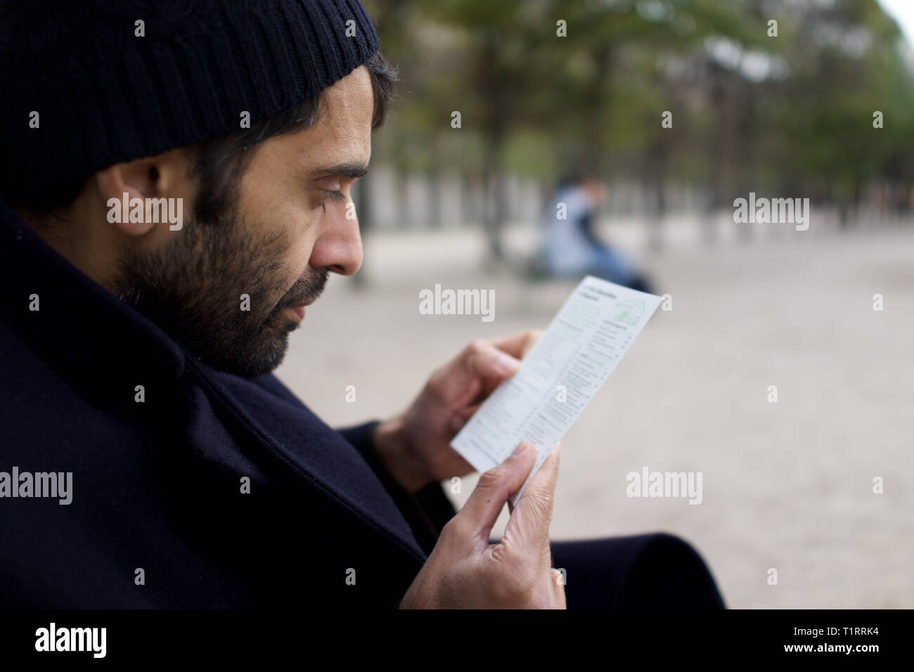 Uomo di Pakistani, Indiana, origine asiatica, seduta in city park, leggere il foglietto - inverno Foto Stock