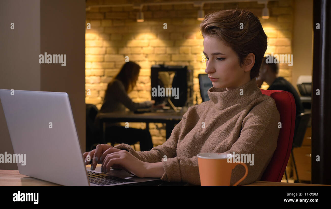 Closeup shoot di giovani attraenti caucasici dipendenti di sesso femminile la digitazione sul computer portatile in ambienti chiusi in ufficio Foto Stock
