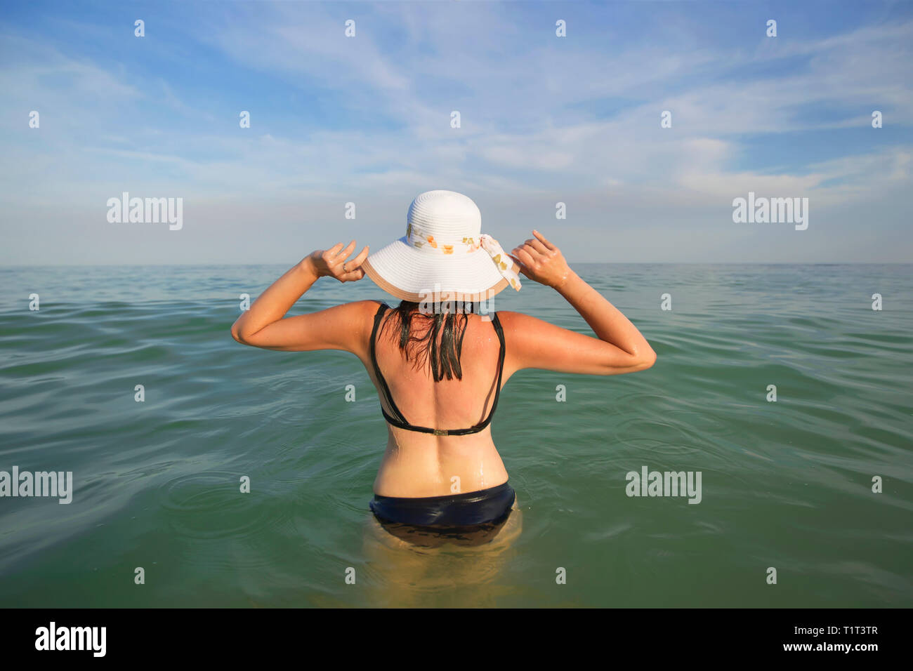 Una donna con un cappello va in acqua di mare. Vacanza sulla costa Foto Stock