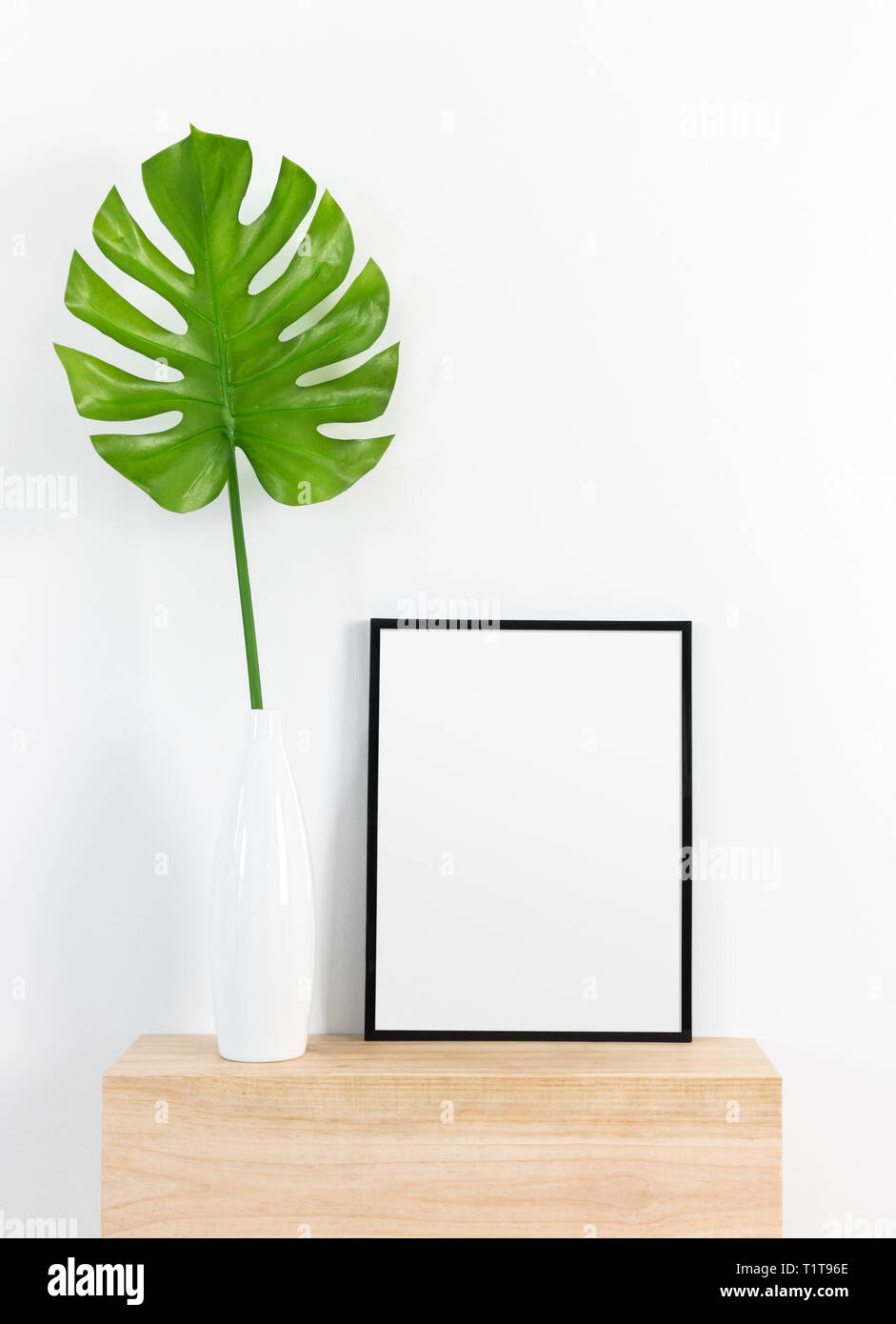 Foglia tropicale in un vaso bianco e cornice nera su una superficie di legno. Home moderno decor. Foto Stock
