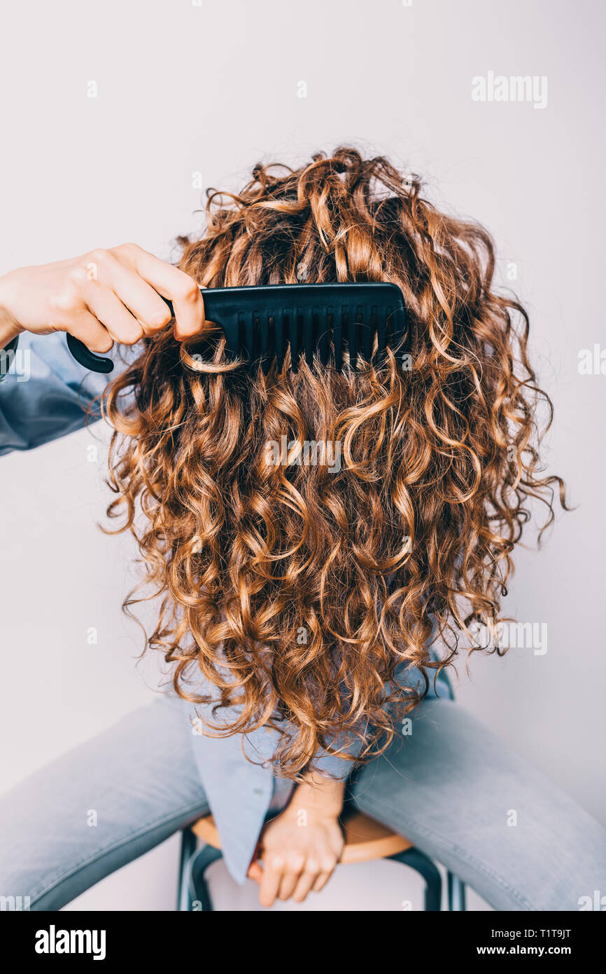 Close-up di testa femmina con spesso lunghi capelli ricci. Giovane donna in maglietta blu è seduto e passando attraverso il pettine lei riccioli. Foto Stock