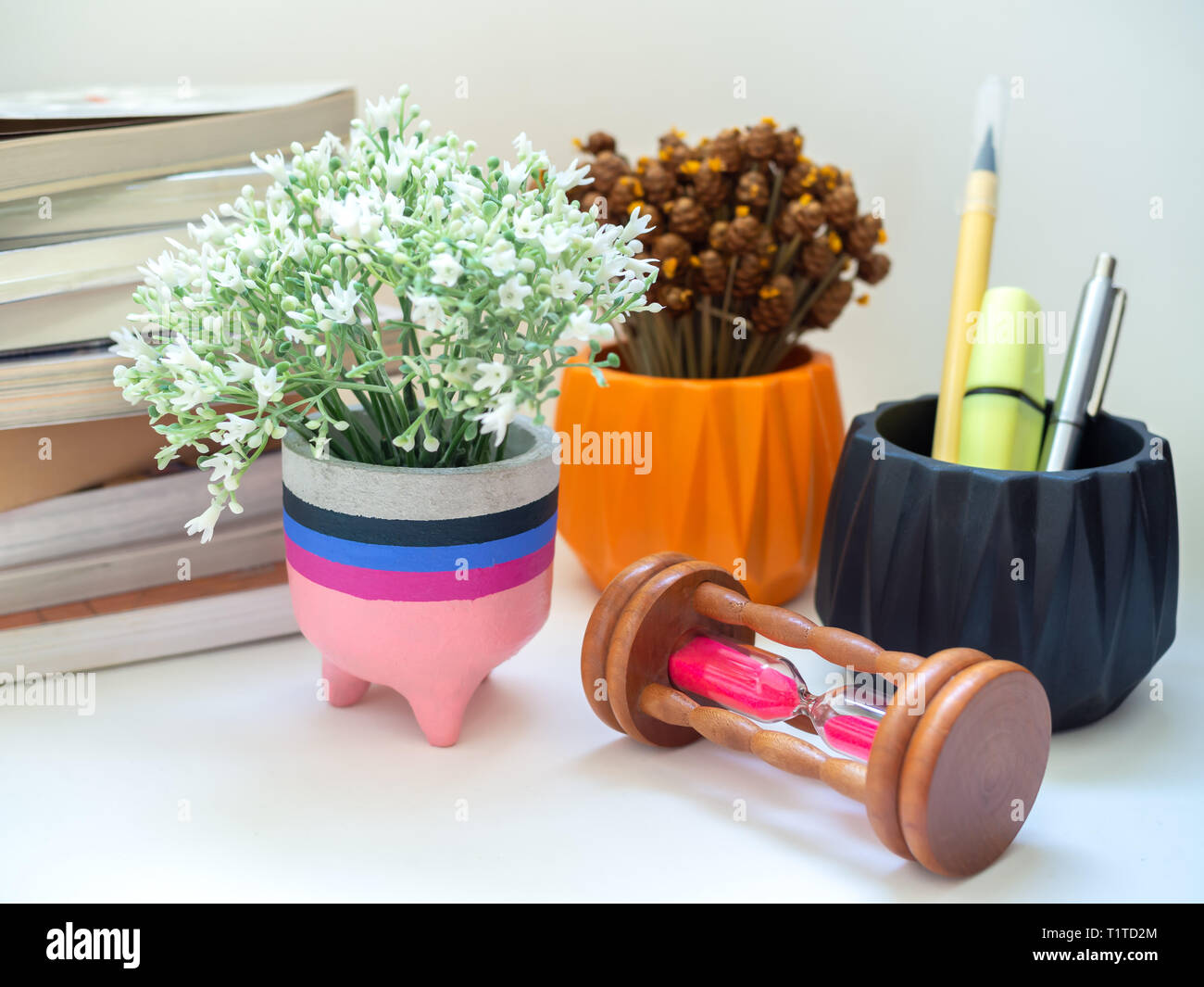 Colorato calcestruzzo moderno piantatrice con fiore, Clessidra e libri su sfondo bianco. moderna scrivania da ufficio decorazione. Foto Stock
