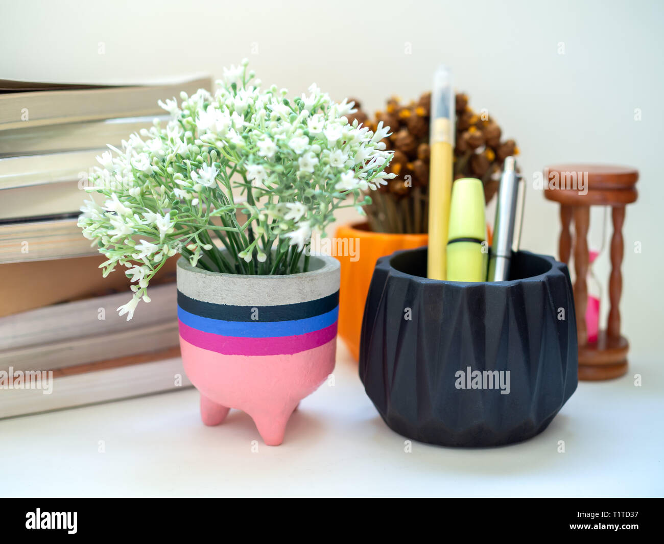 Colorato calcestruzzo moderno piantatrice con fiore, Clessidra e libri su sfondo bianco. moderna scrivania da ufficio decorazione. Foto Stock