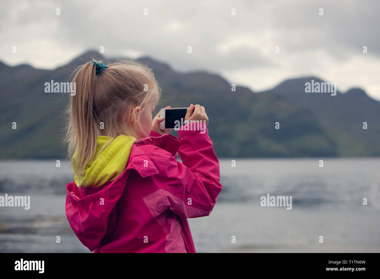 Bambino di prendere una foto di viaggio su un telefono cellulare di un loch e paesaggio in Scozia Foto Stock