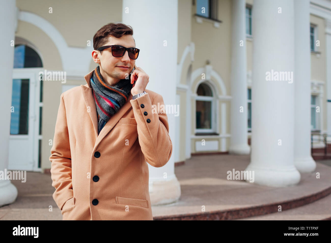Giovane imprenditore elegante utilizza lo smartphone in città. Bel ragazzo indossa abiti classici e accessori. Street fashion Foto Stock