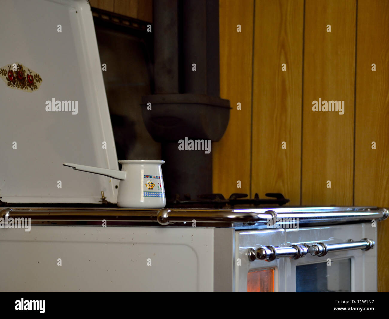 Economico stufa a legna per la cottura, cottura e riscaldamento. White stufa a legna in una cucina di una casa con un caffè turco pentola sul fuoco. Foto Stock