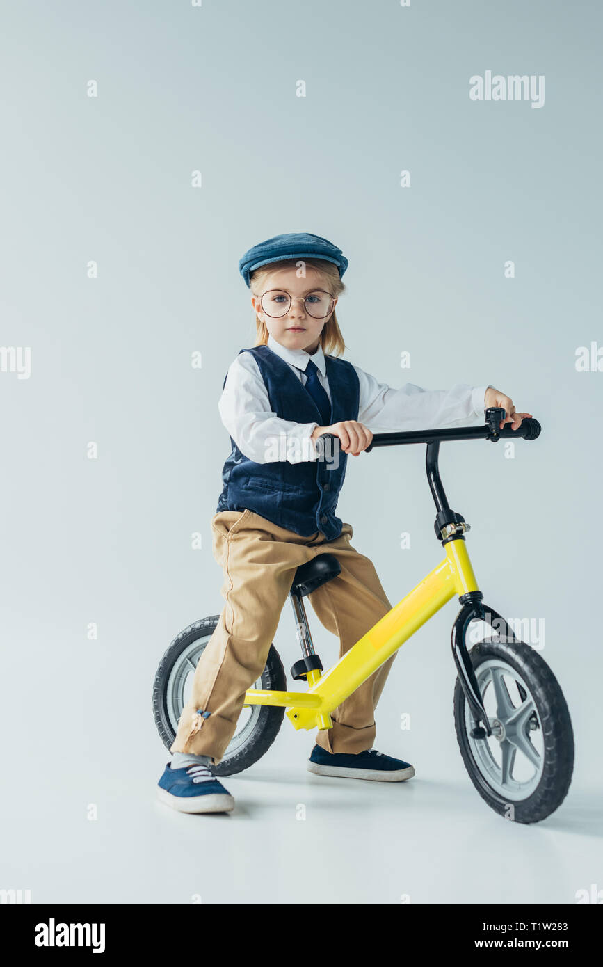 Kid rétro Giubbotto cappuccio e bicicletta equitazione e guardando la fotocamera su sfondo grigio Foto Stock